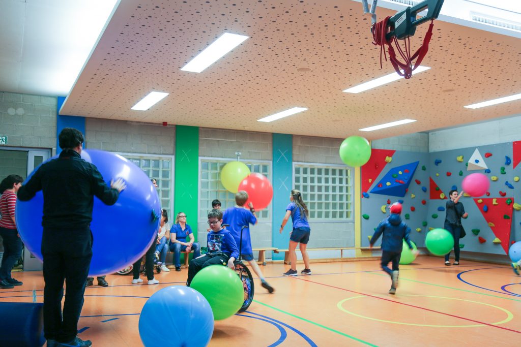 Disabled and non-disabled children, parents and teachers playing with huge colored balls in excercise hall. The balls are bounding up and down.